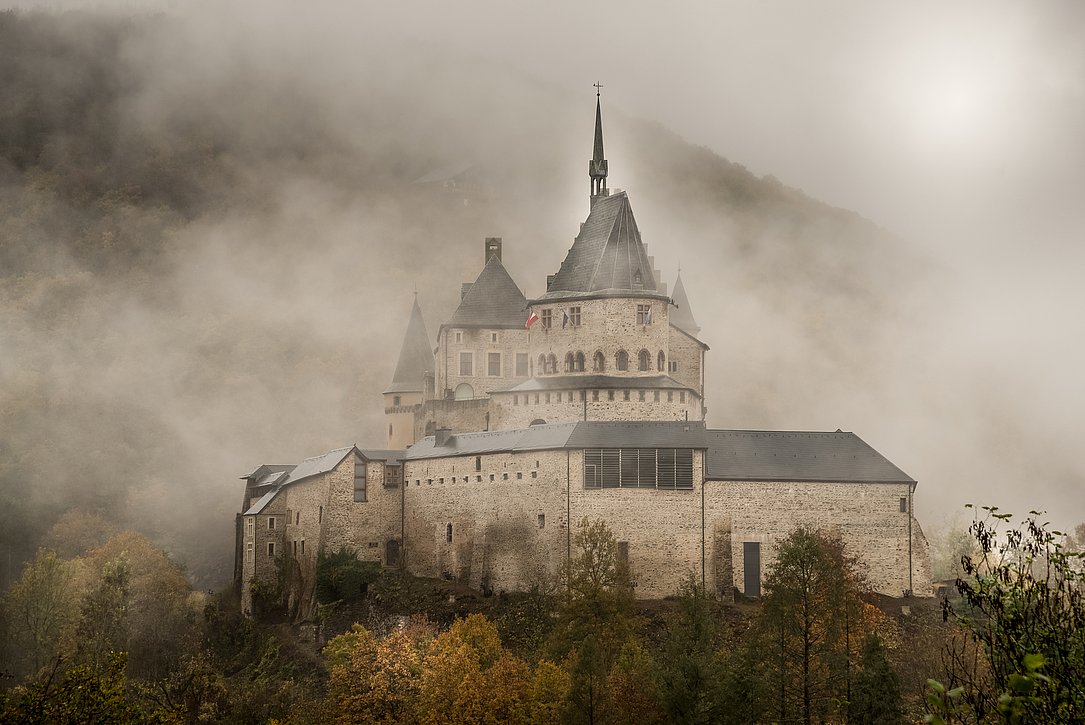 Eine mystische Aufnahme von Schloss Vianden im Nebel, das majestätisch zwischen den Hügeln emporragt.