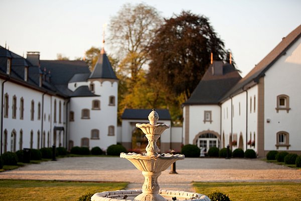 De binnenplaats van Château de Urspelt, met een zonnig uitzicht op een fontein en het hotel dat zich binnenin het kasteel bevindt.