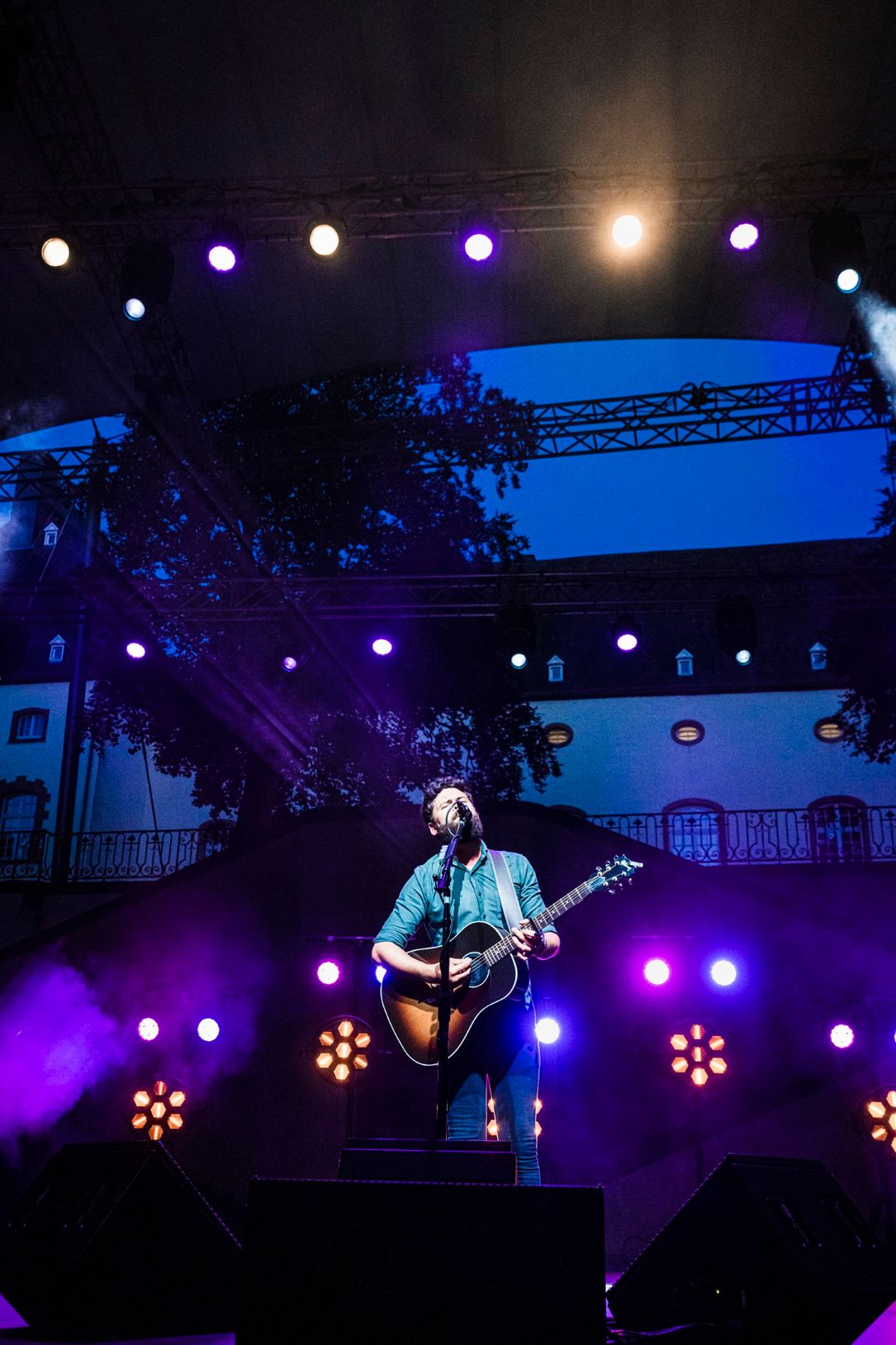 A shot of a singer with a guitar, surrounded by blue-violet lights on the stage of the famous Festival de Wiltz. The singer performing is Passenger. The photo is from 2022.