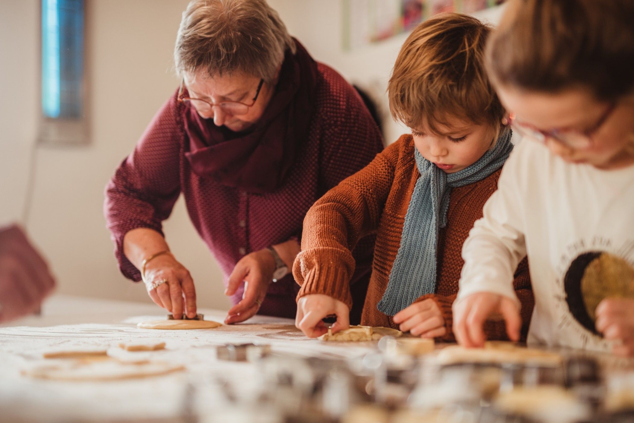 Des enfants et une femme sont assis à une table, ils préparent des biscuits ensemble, et les enfants découpent des formes avec des emporte-pièces.