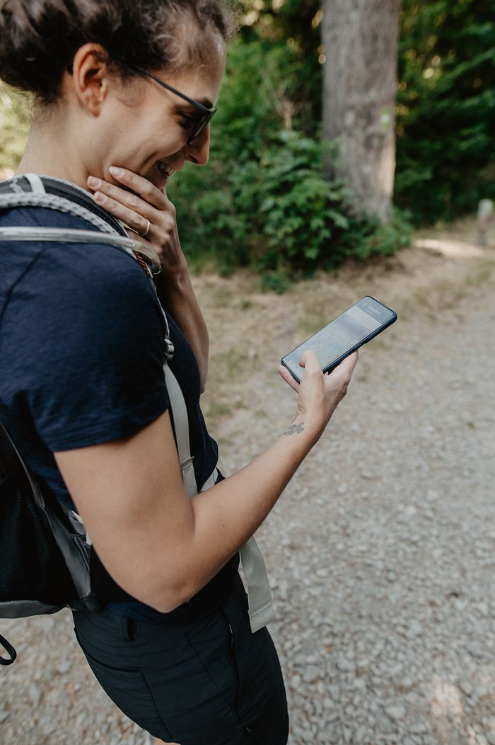 Une personne rit et regarde son smartphone pour trouver le chemin qu'elle emprunte. Elle utilise une application de navigation sur son téléphone.