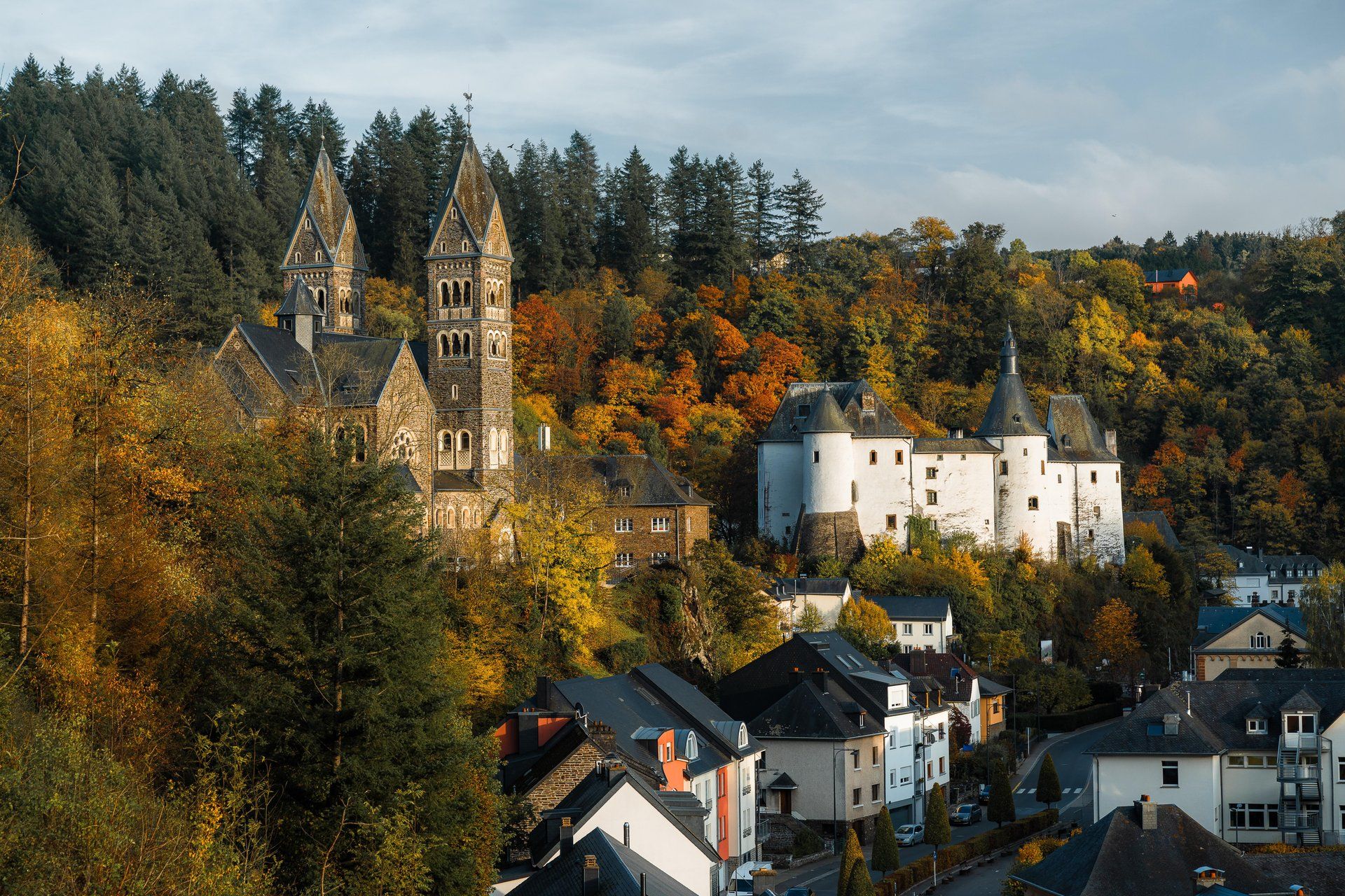 Herbstpanorama der Stadt Clervaux, umgeben von bunten Wäldern im Éislek, Luxemburg.