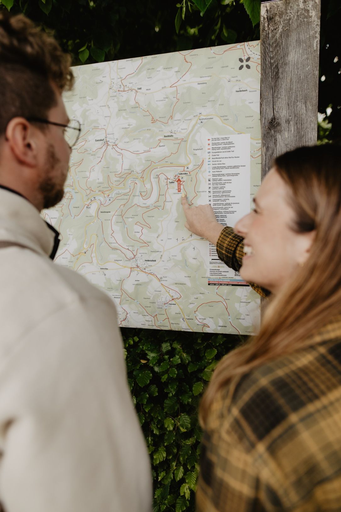 Two people looking at a hiking map panel to plan their route in Éislek