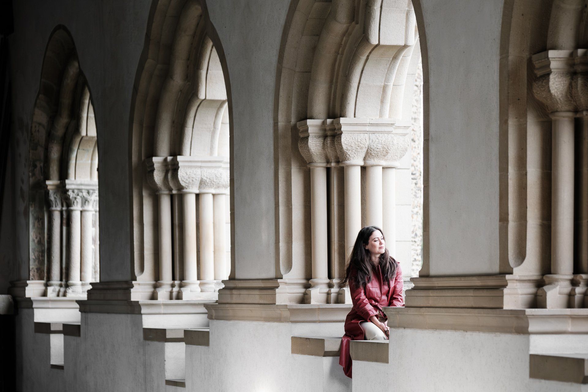 Een foto in de zuilenzaal van kasteel Vianden, waar een vrouw in het rood zit bij een van de ramen en naar buiten kijkt.