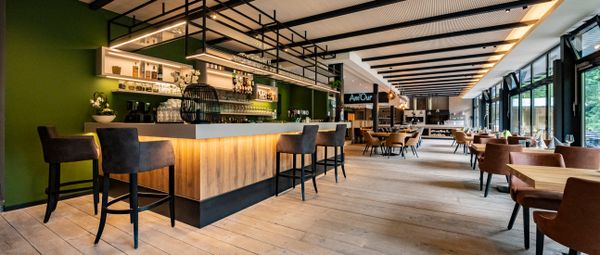 Een stijlvol ingericht restaurant met een toonbank en bar, groene muren, houten accenten en grote panoramische ramen die voor een aangename sfeer zorgen.