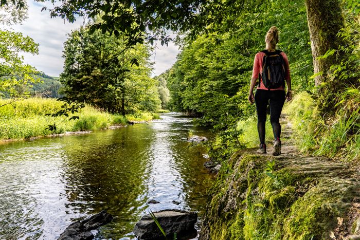 Une randonneuse marche le long de la rivière sur l’Éislek Pad Kalborn, au cœur d’une nature paisible.