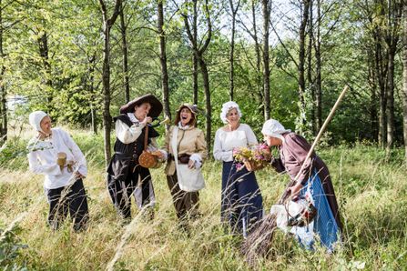 Des personnes déguisées sont présentes sur l'image, toutes portant des vêtements de la même époque historique. Cela montre un moment de la visite guidée animée dans la forêt.
