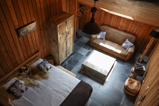 Een bed en een bank in een warme, met hout beklede kamer, van bovenaf gefotografeerd.