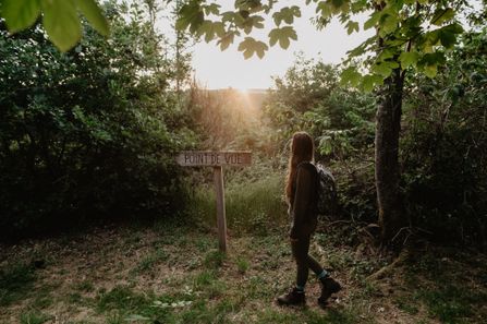 A woman stands at sunset in front of a wooden sign at the Kinneksknäppchen viewpoint in Brandenbourg.