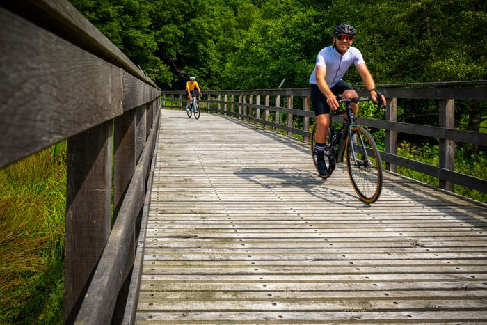 Deux cyclistes roulent sur la piste cyclable PC 20 à Merkholtz, traversant un pont en bois près de la carrière étatique.