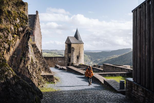 Visitor walking along the stone path inside Bourscheid Castle with tower and view over the Sûre Valley