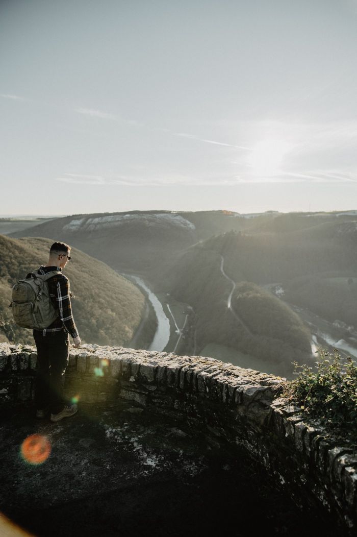 Un homme avec un sac à dos se tient sur une plateforme d'observation en pierre et regarde dans la vallée.