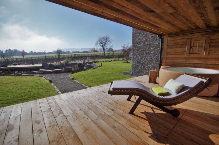 Vue depuis la terrasse d’un des chalets Petry avec un jacuzzi sous un soleil éclatant, au cœur de la nature.