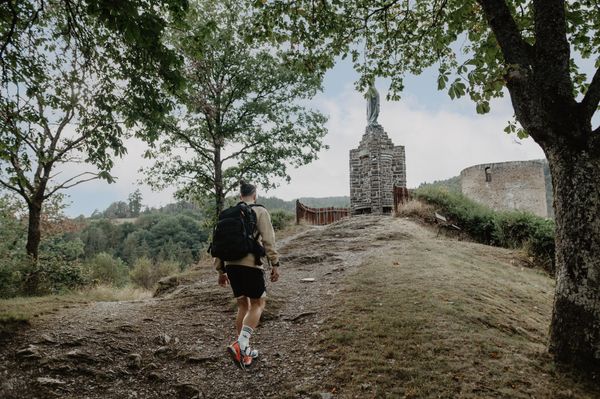 Hiker walking uphill on the Éislek Pad near Esch-sur-Sûre with chapel and trees along the path