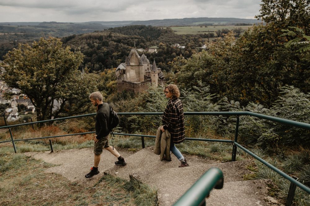 Un couple descend du point de vue du télésiège à Vianden en direction de la ville. En arrière-plan, on peut voir le château de Vianden.