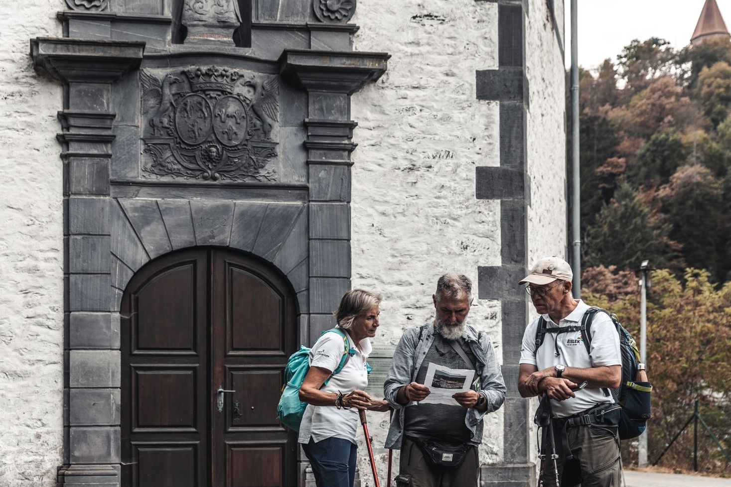 Drei Wanderer bei einer geführten Wanderung in Clervaux, aufgenommen vor einer Kirche.