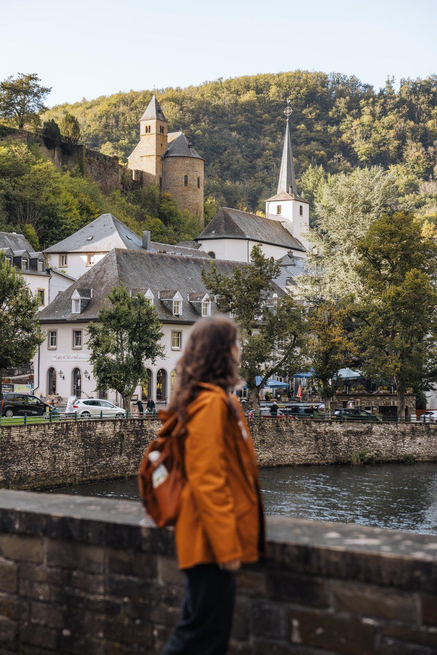 View of Esch-sur-Sûre with church and houses along the Sûre river, surrounded by forested hills