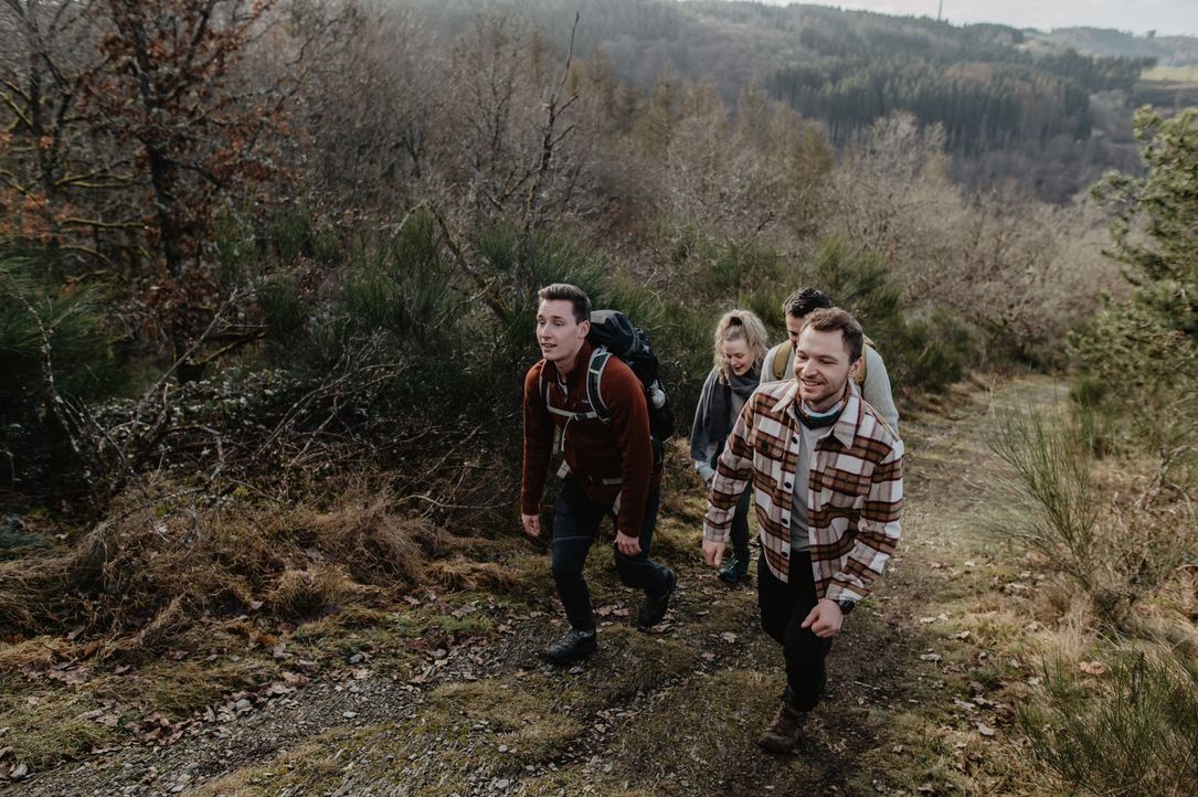 Eine Gruppe junger Leute wandert im Herbst einen Anstieg entlang des Éislek Pad Kautenbach hinauf, umgeben von buntem Laub.