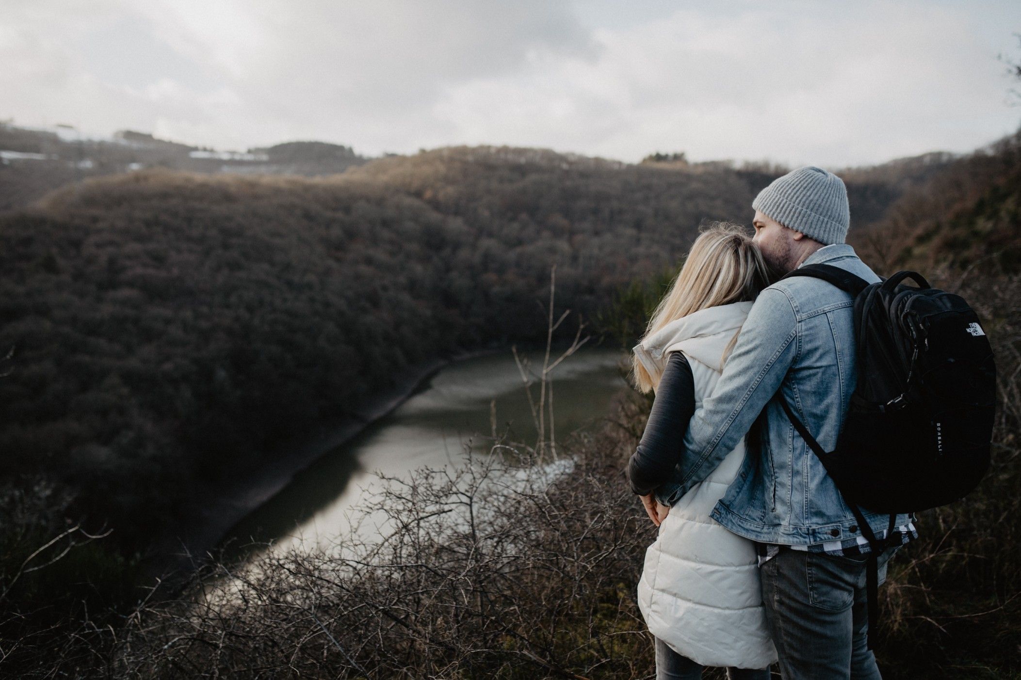 Un couple s’enlace en se tenant sur un point de vue surplombant la rivière et la forêt.
