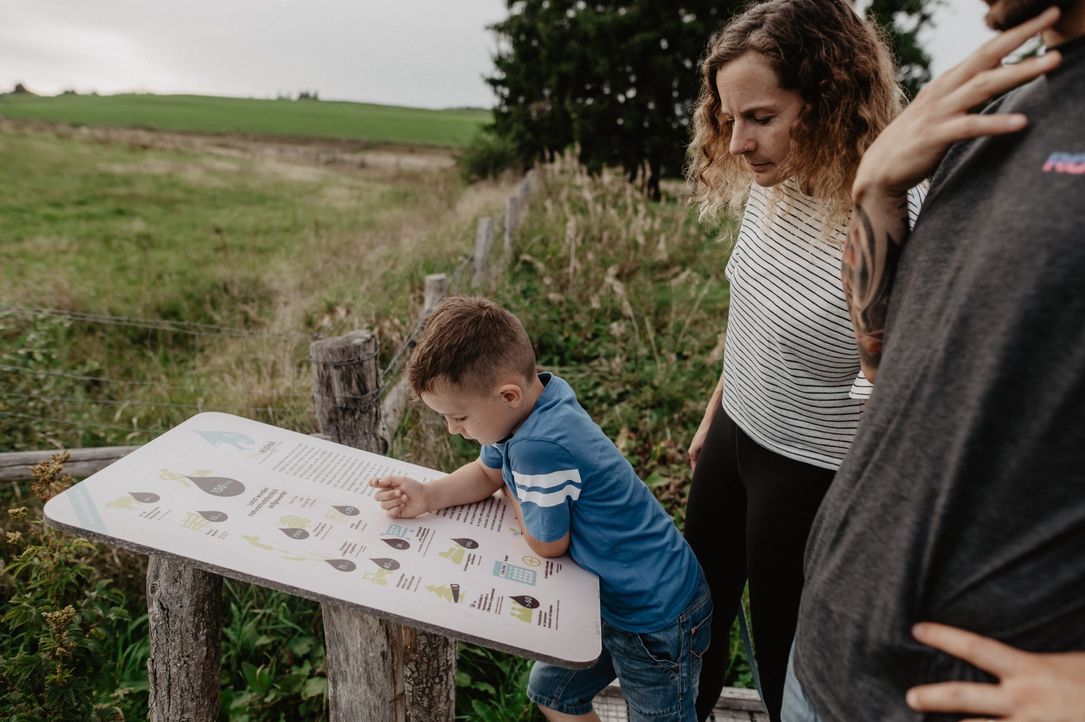 Eine Familie steht vor einer Infotafel im Naturschutzgebiet entlang des Éislek Pad Asselborn.