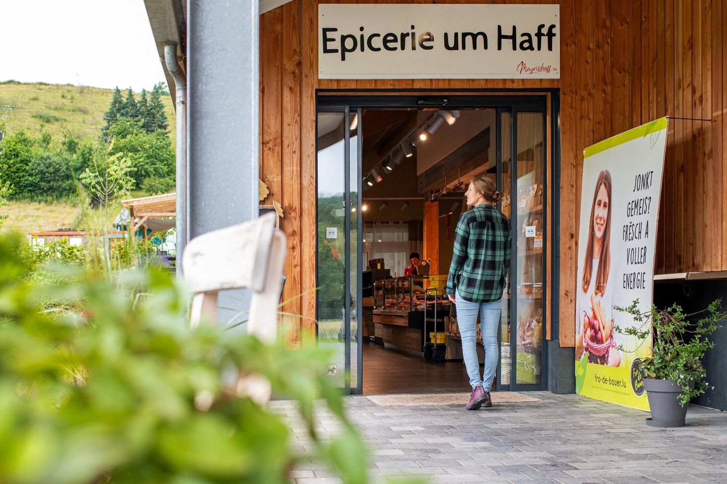 Persoon gaat de boerderijwinkel Epicerie um Haff in op Meyrishaff met houten gevel en ingang