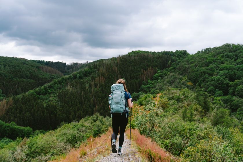 Een vrouw, van achteren gefotografeerd, wandelt met een grote groene rugzak over een bergkam op de Lee Trail.
