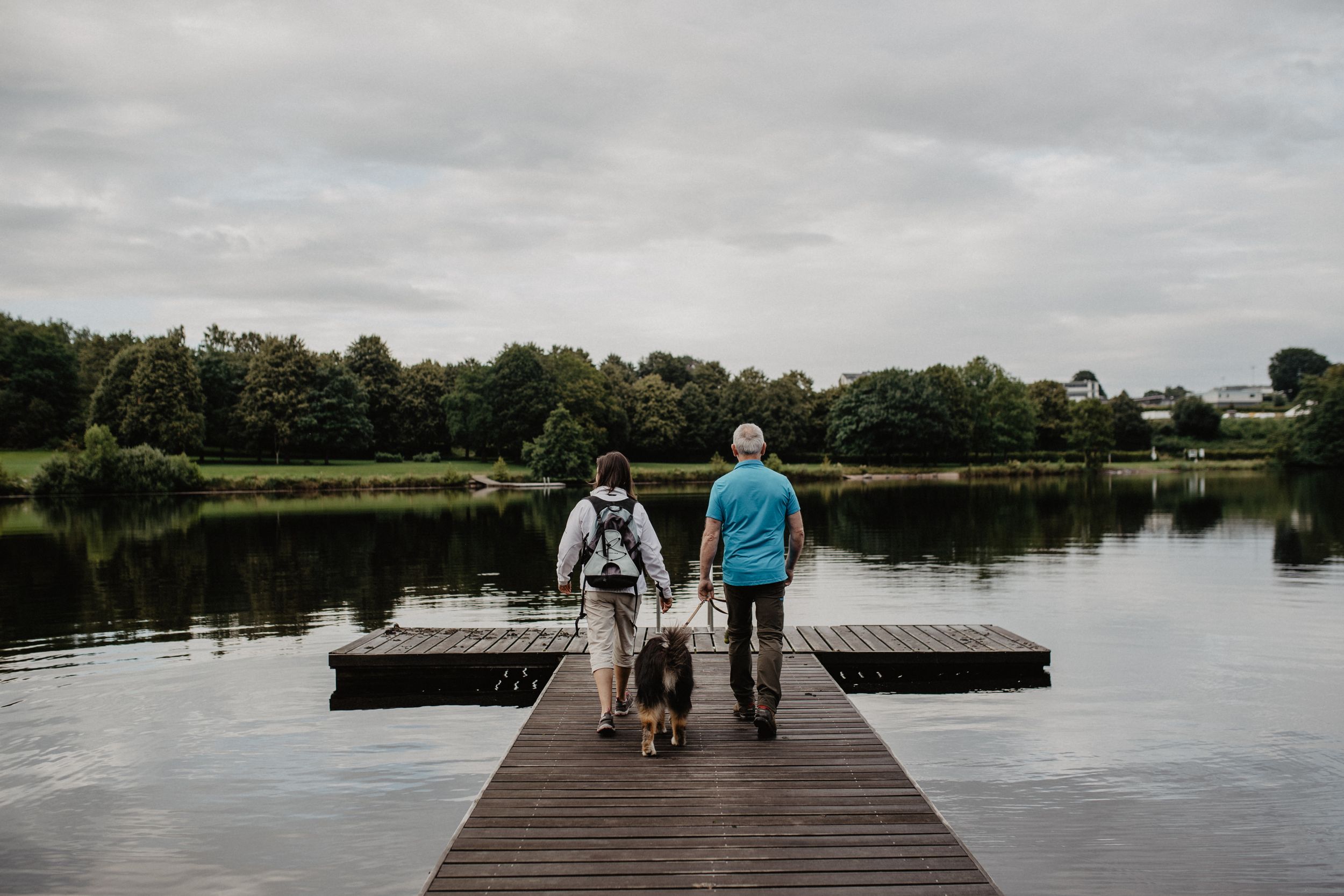 Un couple âgé avec un chien se promène sur une passerelle en bois en direction du lac de Weiswampach.