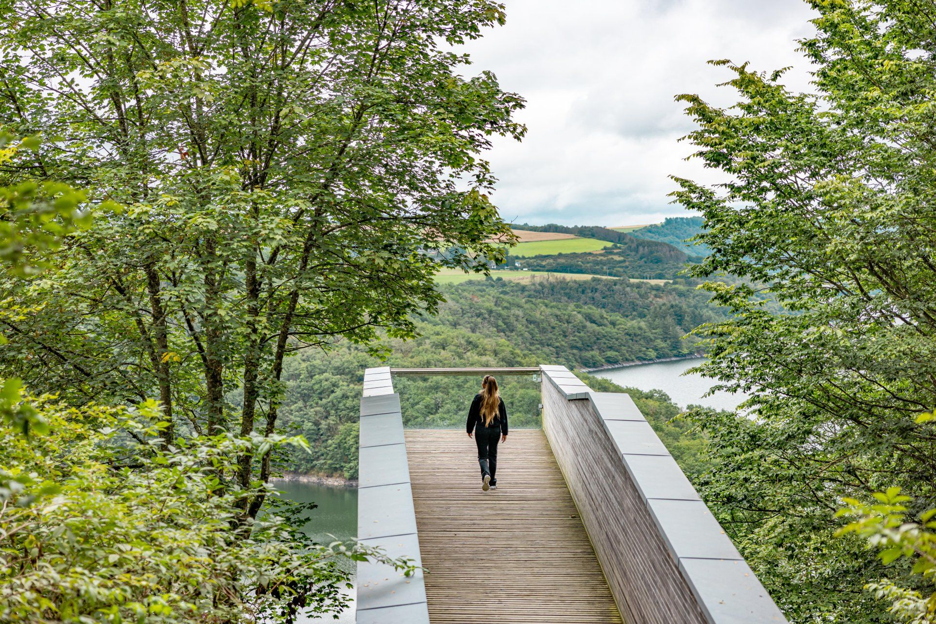 Visiteur sur la plateforme panoramique Burfelt avec vue sur le lac de la Haute-Sûre entouré de forêt