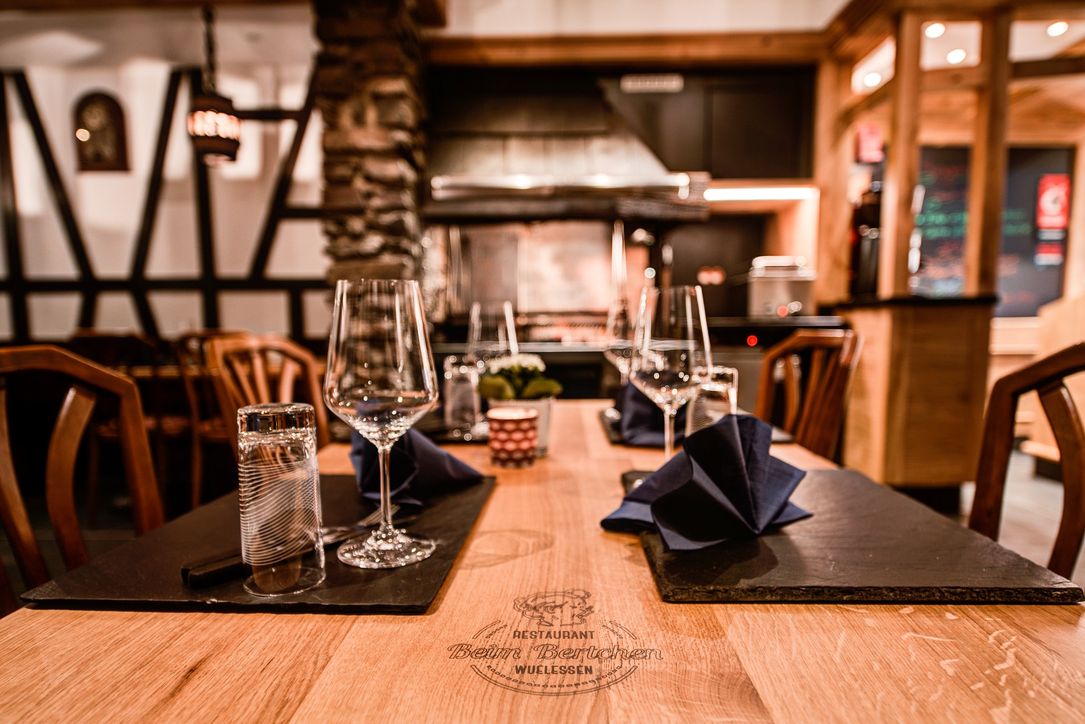 A shot of a table at the restaurant "Beim Bertchen" in Vianden. The venue has a warm and rustic look, with a beautiful wooden table in the foreground, with glasses on top.